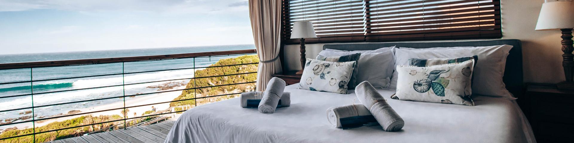 A bed with bed textiles and a view of the sea in the background