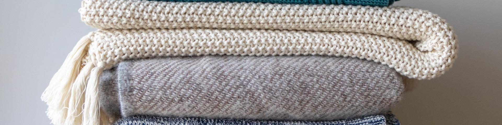 Four blankets and throws of various colours stacked on top of each other